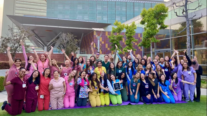 Group photo of over 50 adults wearing colorful, color-coordinated nurses' uniforms posing outside the CHLA main campus building